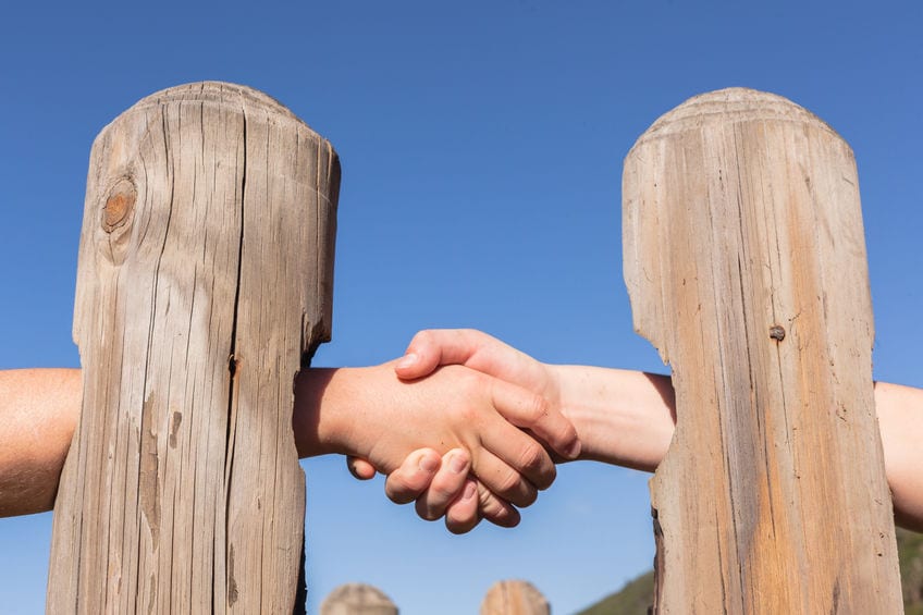 Two people shake hands through holes in a fence
