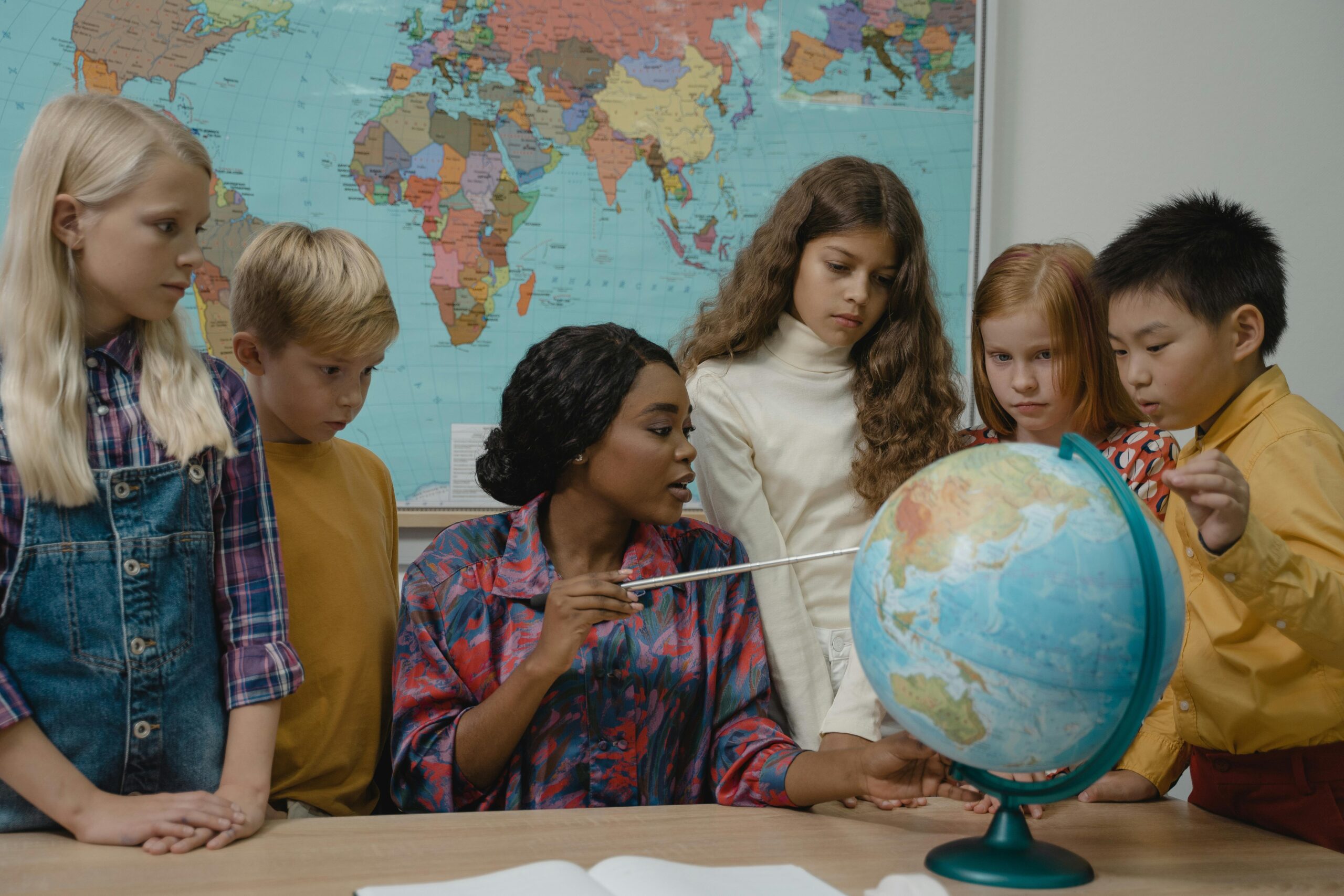 Visual Learning - a teacher points at something on the globe to the students around her